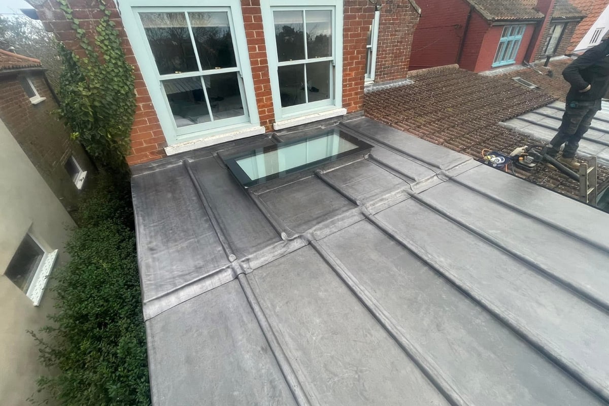A grey flat roof with a rooflight between two buildings