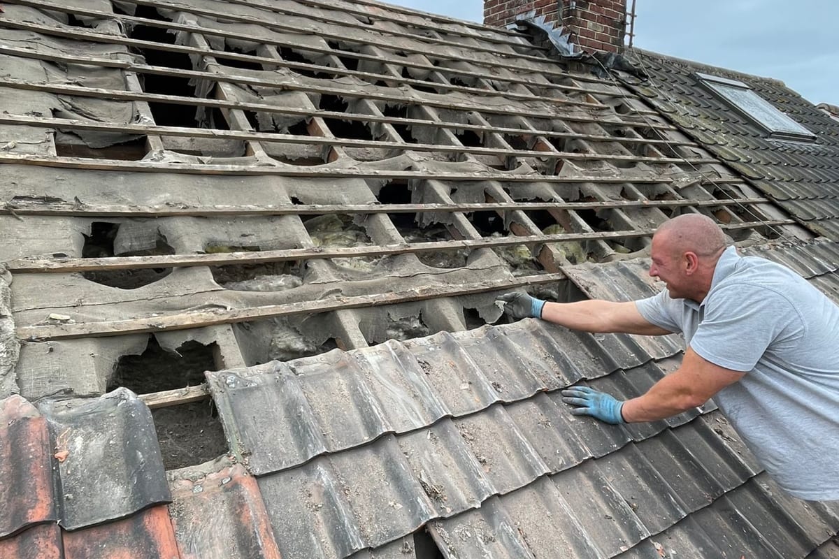 A roofer replacing broken tiles on an old roof
